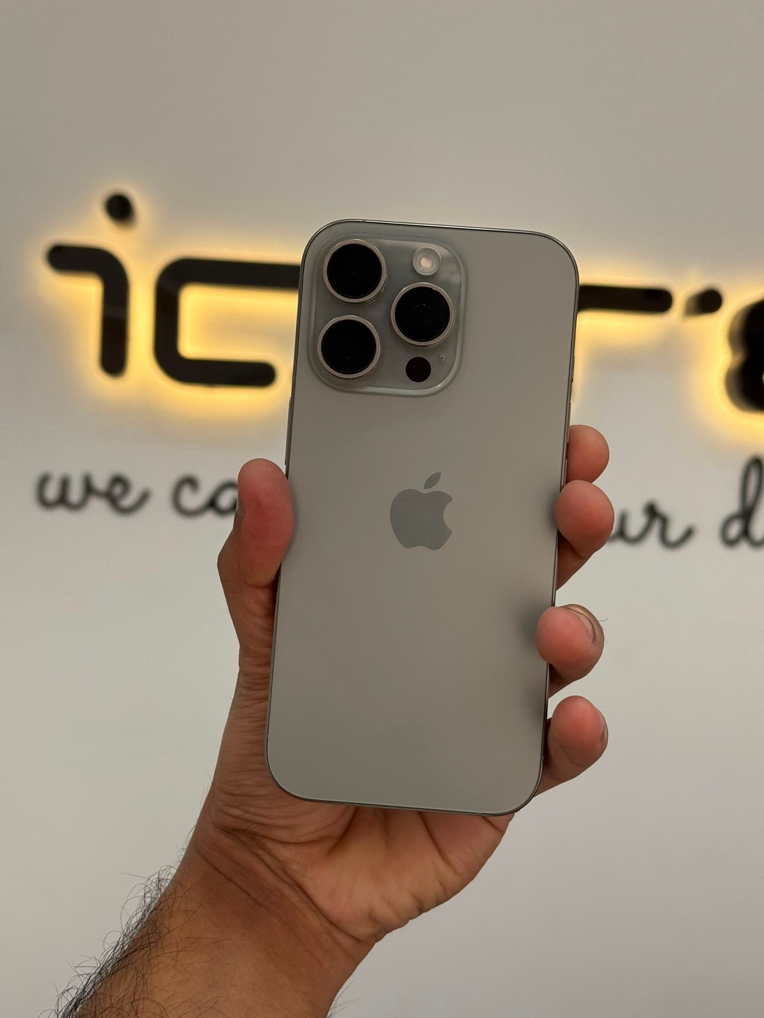 ICARE technician holding a customer's iPhone in front of the illuminated ICARE 'We Care For Your Devices' sign at the Al Gharafa workshop in Doha